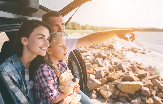 Pausenzeit auf der Urlaubreise, Familie sitzt im geöffneten Kofferraum und guckt auf einen See