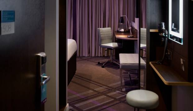Premier Inn Premier Plus room with light up vanity mirror alongside office chair with smart-TV, office table lamp, desk and stools. 